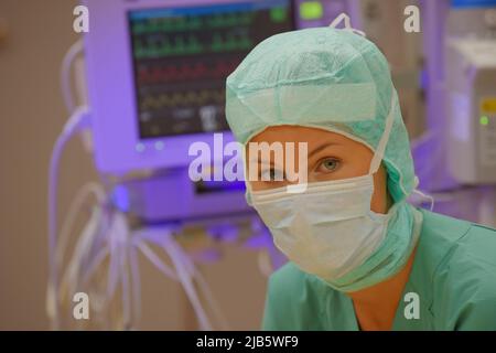 In einem Operationssaal wird eine Krankenschwester aus dem Betanestheater gesehen. Sie wird in grüner steriler medizinischer Kleidung mit einer Gesichtsmaske über ihrem Gesicht gesehen. Stockfoto