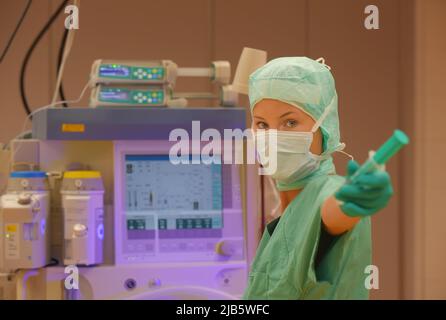 In einem Operationssaal wird eine Krankenschwester aus dem Betanestheater gesehen. Sie wird in grüner steriler medizinischer Kleidung mit einer Gesichtsmaske über ihrem Gesicht gesehen. Stockfoto