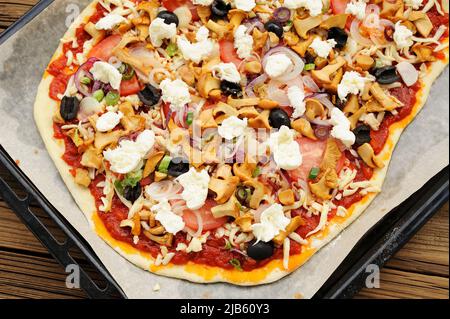 Rohe Pizza al funghi mit Pfifferlingen und Oliven auf Backpapier horizontal Stockfoto