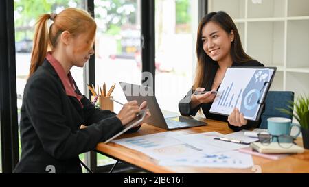 Eine selbstbewusste asiatische Finanzberaterin, die einem weiblichen Geschäftskunden die Umsatzgrafik und das Diagramm präsentiert. Stockfoto