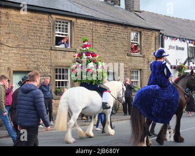 Der König der Castleton Garland mit einem Kranz aus Blumen reitet zu Pferd durch das Dorf während der alten Castleton Garland Ceremony 2022 Stockfoto