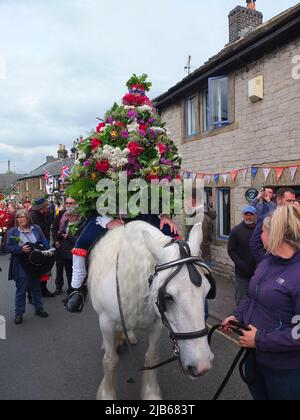 Der König der Castleton Garland mit einem Kranz aus Blumen reitet zu Pferd durch das Dorf während der alten Castleton Garland Ceremony 2022 Stockfoto