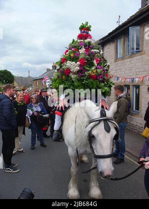 Der König der Castleton Garland mit einem Kranz aus Blumen reitet zu Pferd durch das Dorf während der alten Castleton Garland Ceremony 2022 Stockfoto