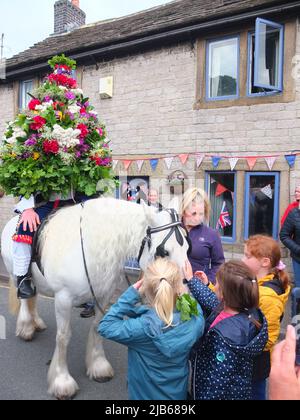 Der König der Castleton Garland mit einem Kranz aus Blumen reitet zu Pferd durch das Dorf während der alten Castleton Garland Ceremony 2022 Stockfoto