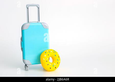 Ein blauer Koffer auf Rädern und ein gelber aufblasbarer Donut stehen auf weißem Hintergrund. Stockfoto