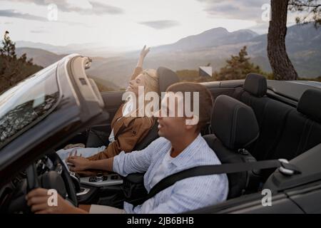 Glückliches junges Paar in der Liebe fahren dachlos Cabrio Auto hält Hände, Blick auf die Berge Stockfoto