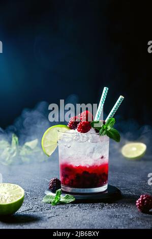 Cocktail mit Rum oder Vodka, Soda, Himbeer- und Brombeerpüree, Limette und Minze im Glas mit Rauch auf dem dunkelgrauen Hintergrund Stockfoto