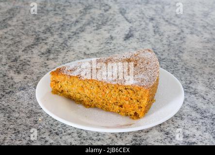 Vorderansicht, Nahaufnahme eines Stücks frischer Karottenkuchen mit Puderzucker bestreut auf weißem Marmorhintergrund. Feuchter, hausgemachter Weihnachtskuchen. Stockfoto