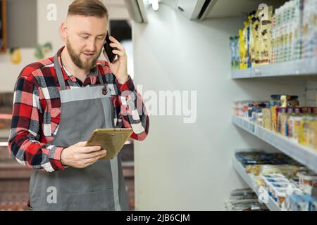 Nahaufnahme eines kaukasischen männlichen Arbeiters, der im Supermarkt steht und auf einem Tablet tippt. Junger fröhlicher Mann Lebensmittelgeschäft Assistent bei der Arbeit Klopfen auf Gerät in Innenräumen Stockfoto