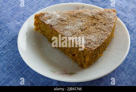 Nahaufnahme und Draufsicht auf ein Stück gesunden Karottenkuchen mit Zuckerstauben auf der Oberseite, isoliert auf dunklem Hintergrund. Weicher, feuchter hausgemachter Kuchen, Kopierraum. Stockfoto