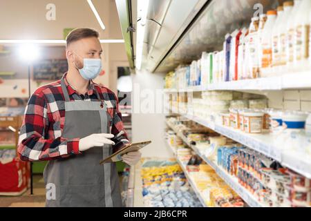 Selbstbewusster Supermarktangestellter in Schutzmaske, der mit einem digitalen Tablet, Technologie und Arbeit arbeitet Stockfoto