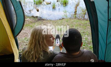 Rückansicht eines Paares, das im Zelt in der Nähe des wunderschönen Flusses, des Sees, sitzt Stockfoto