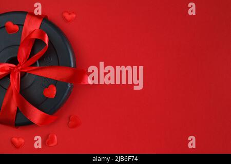 Hantelscheibe mit Band als Liebesgeschenk zum Valentinstag. Gesunde Fitness Flat Lay Komposition, Gym Workout Konzept mit Copy Space. Stockfoto