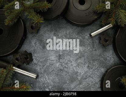 Schwere Hanteln Hantelscheiben und Christbaumzweige. Gesunde Lebensweise Weihnachtszeit Zusammensetzung. Festliches Flat Lay-Konzept mit Copyspace. Stockfoto