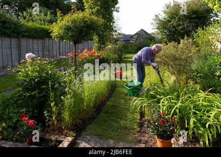 Hampshire, England, Großbritannien. 2022. Frau bereitet den Boden für neue sommerblühende Pflanzen in einem englischen Landgarten vor Stockfoto