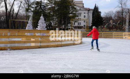 Junge mit roter Jacke, Schlittschuhlaufen tagsüber, Spaß haben und auf der Eisbahn studieren. Stockfoto