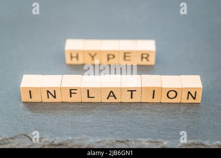 Das Wort Inflation und Hyper im Hintergrund Text auf einem Schiefer mit einem Holzwürfel geschrieben. Stockfoto