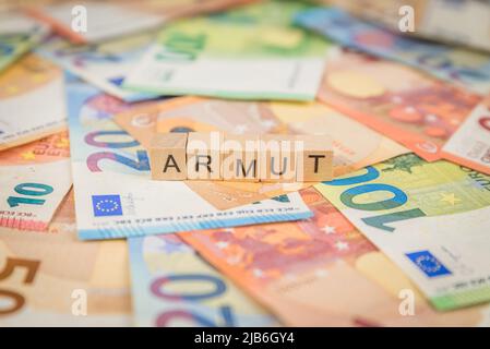 Das Wort Armut - auf Deutsch für Arme - auf Banknoten Euro-Scheine mit Holzwürfel geschriebener Text Stockfoto