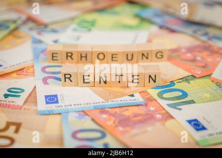 Das Wort Renten - auf Deutsch für Rente - und Erhoehung - auf Deutsch für Raise - im Hintergrund auf Euro-Banknoten geschrieben mit Holzwürfeln tex Stockfoto