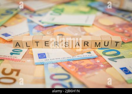 Das Wort Altersarmut - auf Deutsch für Altersarmut - steht auf Euro-Banknoten mit Holzwürfeltext Stockfoto