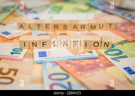 Das Wort Inflation - und Altersarmut - im Deutschen für Altersarmut - im Hintergrund auf Banknoten Euro-Scheine geschrieben mit Holzwürfeln Text Stockfoto