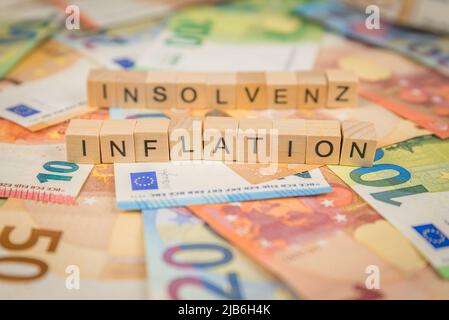 Das Wort Inflation und Insolvenz - im Deutschen für Insolvenz - im Hintergrund auf Banknoten Euro-Scheine geschrieben mit Holzwürfeltext Stockfoto