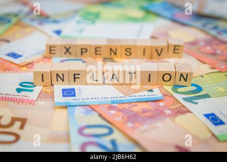 Das Wort Inflation und teuer im Hintergrund auf Banknoten Euro-Noten mit Holzwürfel geschrieben Text Stockfoto