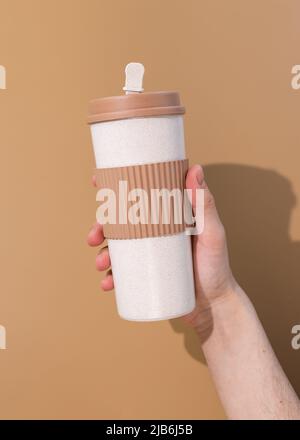 Nachfüllbarer Becher in Young mans Hand auf beigem Hintergrund. Konzept der plastikfreien und Zero Waste Living Stockfoto