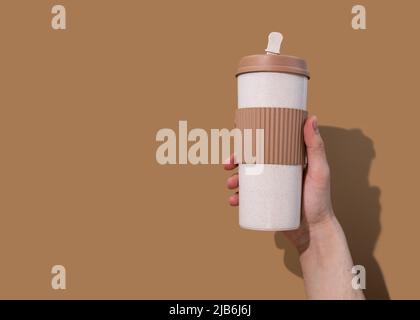 Nachfüllbarer Becher in Young mans Hand auf beigem Hintergrund. Konzept der plastikfreien und Zero Waste Living Stockfoto
