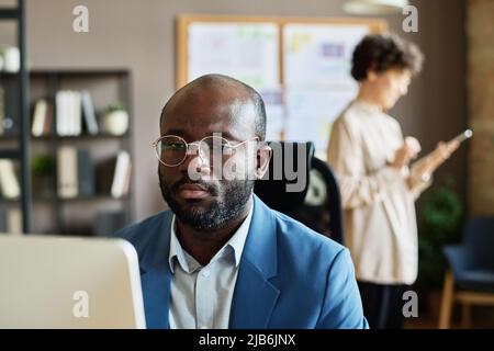 Afrikanischer junger Geschäftsmann in Brillen, der im Büro am Computer arbeitet Stockfoto