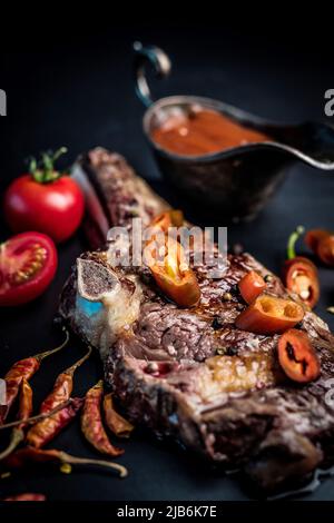 Gegrilltes, heißes Ribeye-Steak auf Knochen mit würziger Sauce Stockfoto