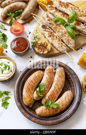 Sommerparty Essen. Grillgerichte. Verschiedene grillwürste mit frischen Kräutern und Gewürzen auf Marmorplatte. Stockfoto