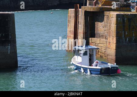 Ein blau-weißes Hummerboot mit einer kleinen überdachten Ruderstation verlässt den Innenhafen von Porthleven und fährt auf das Meer hinaus Stockfoto