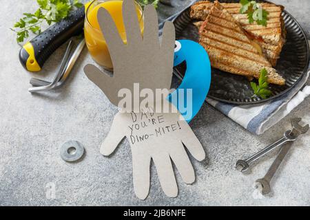 Alles gute zum Vatertag. Vatertag Karte Dinosaurier und Heimwerker Frühstück für Vater auf grauen Stein Tisch. Stockfoto