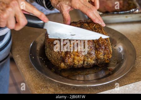 Eine Frau, die einen großen Rinderbraten mit Prime Rib aufschneiden, der von einem Gourmet-Koch für ein Weihnachtsessen im Ofen gebacken und gebraten wurde Stockfoto