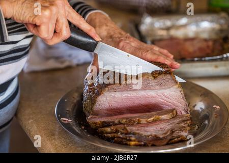 Eine Frau, die einen großen Rinderbraten mit Prime Rib aufschneiden, der von einem Gourmet-Koch für ein Weihnachtsessen im Ofen gebacken und gebraten wurde Stockfoto