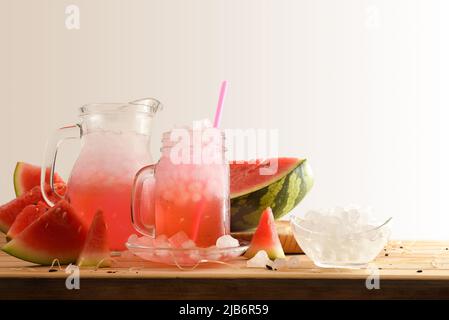Glas und Krug mit natürlichem Wassermelonengetränk mit viel Eis auf einem Holztisch mit Früchten um und isoliertem Hintergrund. Vorderansicht. Horizontal Stockfoto