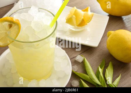 Hintergrund mit Detail von Zitronengetränk mit viel Eis auf Holztisch mit Obst und einer Schüssel mit Eis. Erhöhte Ansicht. Horizontale Zusammensetzung. Stockfoto