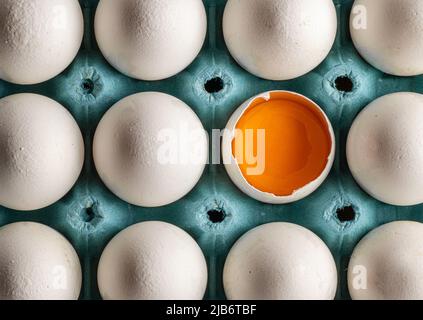 Frische Bio-Hühnereier in Eierschale angeordnet. Halb gebrochenes Ei mit Eigelb sichtbar Stockfoto