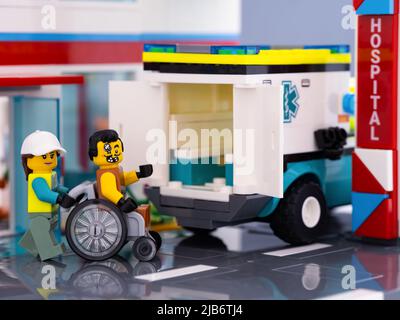 Tambow, Russische Föderation - 11. Februar 2022 Ein Lego-Sanitäter-Minifigur, der einen Rollstuhl mit einem Lego-Patienten, der darin sitzt, in einen Krankenwagen schiebt Stockfoto