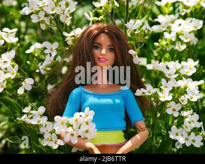 Tambow, Russische Föderation - 30. April 2022 Eine brünette Barbie-Puppe, die an sonnigen Tagen unter weißen Blumen im Freien steht. Stockfoto