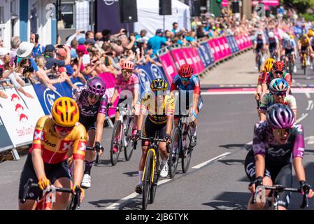 Radsportler des Pelotons überqueren die Ziellinie in der Maldon High Street beim Radrennen RideLondon Classique Stage 1, Essex, Großbritannien. Coryn Labecki Mitte Stockfoto