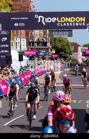 Radsportler des Pelotons überqueren die Ziellinie in der Maldon High Street beim Radrennen RideLondon Classique Stage 1, Essex, Großbritannien Stockfoto