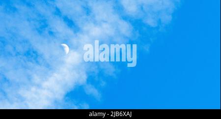 Ein Halbmond in einem blauen Himmel, der durch eine Dampfdampfspur rast Stockfoto