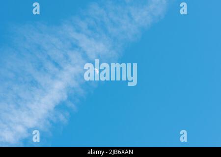 Ein Halbmond in einem blauen Himmel, der durch eine Dampfdampfspur rast Stockfoto