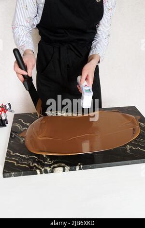 Nahaufnahme Hände von professionellen weiblichen Konditorinnen Kochen Dessert Messung der Temperatur von Schokolade. Prozess des Temperierens von süßer Schokolade Stockfoto