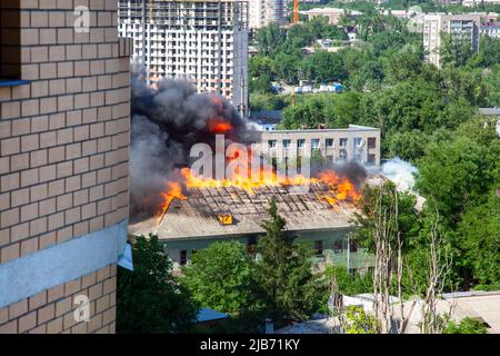 Ein Feuer in einem alten verlassenen Haus, ein Blick aus dem Fenster eines benachbarten Hochhauses. Stockfoto