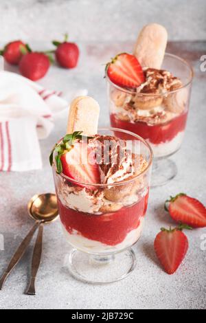 Erdbeere Tiramisu. Traditionelles italienisches Dessert Tiramisu im Glas mit frischen Erdbeer- und Minzblättern auf altem grauen Beton-Hintergrund-Tisch Backgro Stockfoto