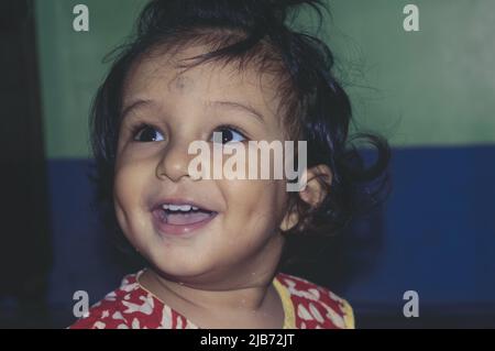 Baby lächelt und schaut mit glücklichen Augen aus der Nähe auf. Liebenswert hübsch indisch glücklich Baby Portrait. Alter ein Jahr sechs Monate. Glückliche Kindheit Und Kinderbetreuung Stockfoto