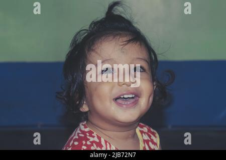 Baby lächelt und schaut mit glücklichen Augen aus der Nähe auf. Liebenswert hübsch indisch glücklich Baby Portrait. Alter ein Jahr sechs Monate. Glückliche Kindheit Und Kinderbetreuung Stockfoto